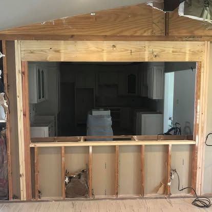 A partially framed interior wall opening in a room under construction, revealing a kitchen with white cabinetry.