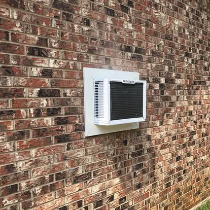 A white window air conditioning unit mounted through an exterior brick wall.