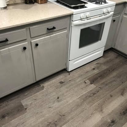 Light gray kitchen cabinets beside a white stove on a floor with gray wood-look planks.