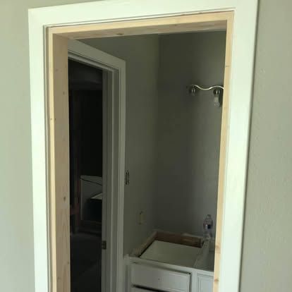 A wooden door frame being installed in a doorway, with a bathroom vanity and light fixture visible in the reflection.