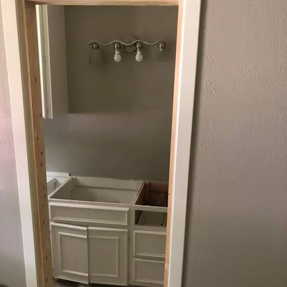 A doorway looks into a bathroom featuring a partially installed white cabinet vanity and a three-bulb light fixture.