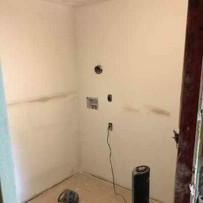 An unfinished laundry alcove featuring wall-mounted water hookups, a drain pipe, and an electrical outlet.