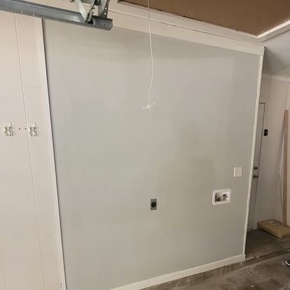 A neutral-colored interior wall features a single electrical outlet and a washing machine hookup box.
