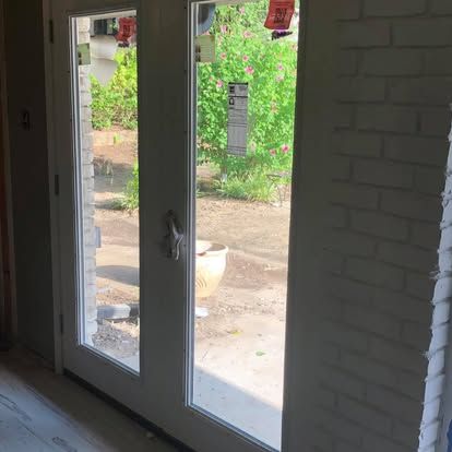 White double doors with glass panels look out onto a yard with green plants and a white planter.