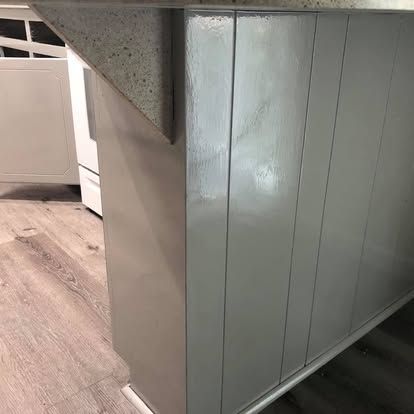 A close-up of a kitchen island corner with gray vertical paneling and a light speckled countertop over wood-look flooring.