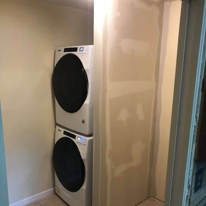 Stacked white Whirlpool laundry machines in an unfinished room with drywall and taped seams.