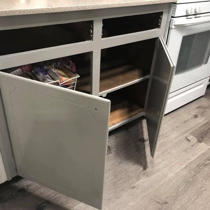 Open grey kitchen cabinets with visible shelves and a wire organizer, positioned next to a white stove.