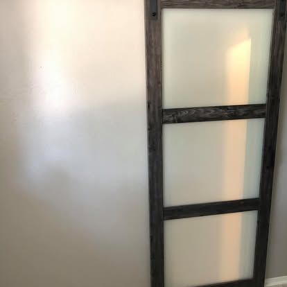 A vertical door with a dark, stained wood frame and three rectangular panels of frosted, semi-transparent glass.