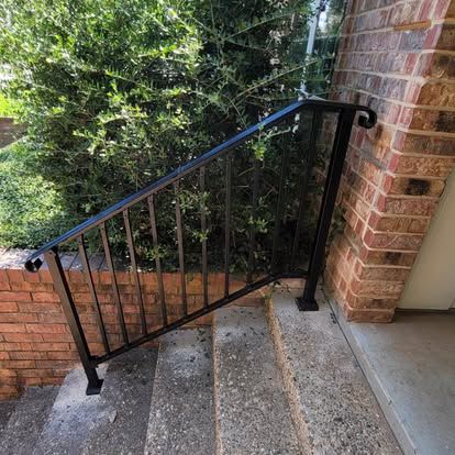 Black metal handrail installed along concrete steps next to a brick wall and green shrubs.