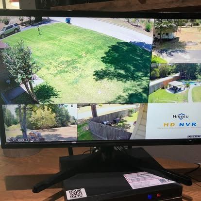 A monitor displaying a multi-view Hiseeu security camera feed of a residential property exterior, including a lawn and yard.