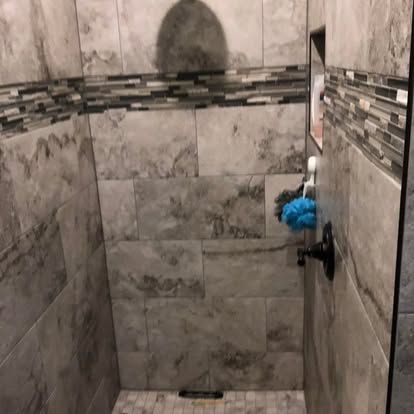 A walk-in shower with gray marbled tiles, a decorative accent border, a built-in recessed shelf, and a black faucet.