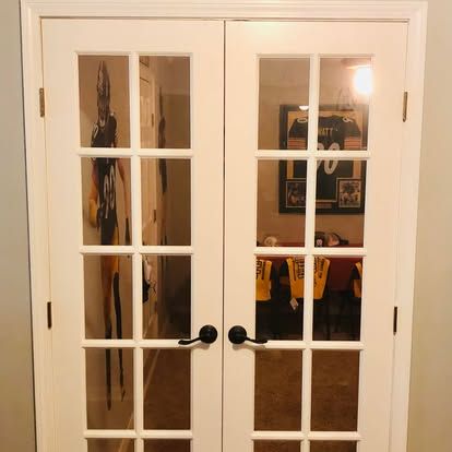 A pair of white French doors with glass panes reflecting a room decorated with sports memorabilia.