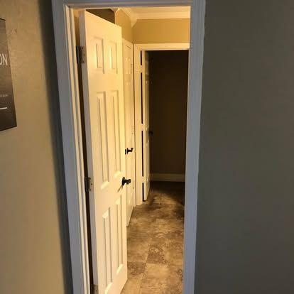 A white paneled door stands slightly ajar, leading into a hallway with tiled floors and another open doorway beyond.