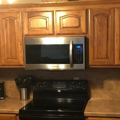 A stainless steel over-the-range microwave sits between oak cabinets above a black electric stove in a kitchen.