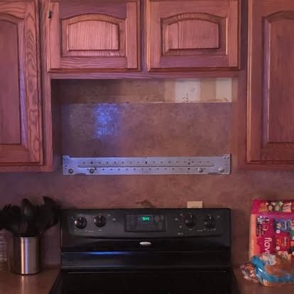 A kitchen stove featuring a metal mounting bracket installed on the wall below a set of wooden cabinets.