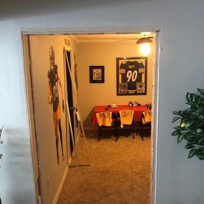 A doorway leads to a room decorated with Pittsburgh Steelers memorabilia, including a wall mural, jersey, and red table.