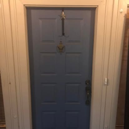 A blue, six-panel door with a star decoration, a brass door knocker, and a dark handle, framed in cream-colored trim.