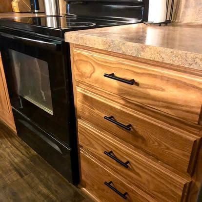 A black oven sits next to a wooden cabinet with four drawers, each featuring a long, black, horizontal handle.