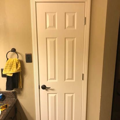 A six-panel white door with a black handle in a bathroom, positioned next to a towel ring with yellow and black towels.