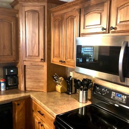 A kitchen corner with wooden cabinets, a stainless steel microwave, a black stove, and a coffee maker on the counter.