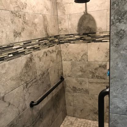 A tiled shower with a black safety grab bar, a decorative mosaic accent stripe, and a black showerhead.
