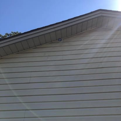 A close-up view of the exterior of a beige-sided house, showing the roofline and a small, circular mounted security camera.