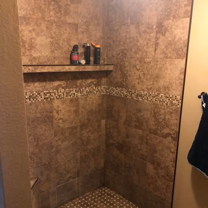 A tiled walk-in shower with a shelf containing three bottles, accented by a horizontal decorative mosaic tile border.