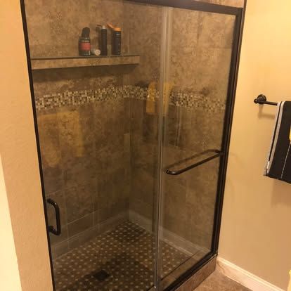 A walk-in shower with brown tiled walls, a glass door with a black frame, and a built-in shelf containing toiletries.