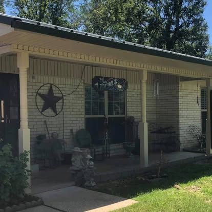 A covered porch of a light brick house featuring a metal roof, a decorative star, and a hanging sign.