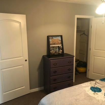 A dark wood dresser sits against a gray wall between two white doors, with a framed picture on top and part of a bed.