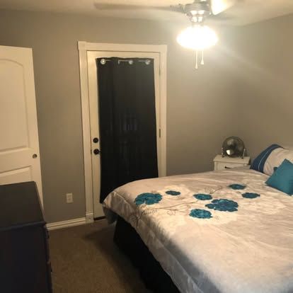 A gray bedroom featuring a bed with a floral comforter and blue pillows, a doorway with black curtains, and a ceiling lamp.