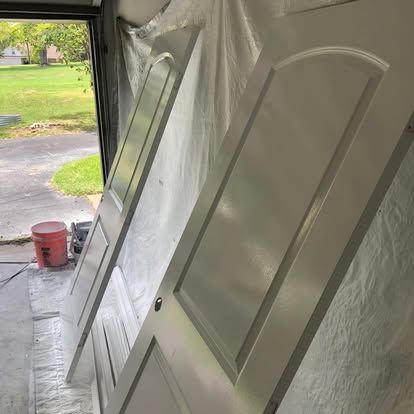 Two freshly painted white doors leaning against a wall in a garage, with a red paint bucket nearby.