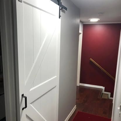 A white barn-style sliding door in a hallway next to a room with dark red walls, a wooden handrail, and hardwood floors.