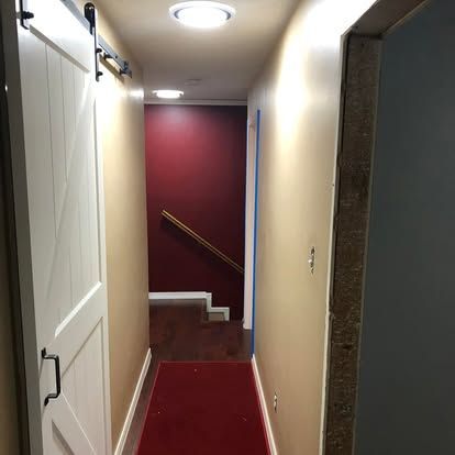 A narrow hallway with a white barn door, tan walls, red carpeting, and a distant maroon wall at the top of stairs.