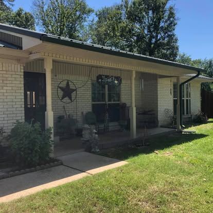 A single-story white brick house with a covered front porch, a star decoration on the wall, and green lawn.