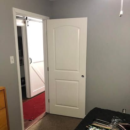 A room with grey walls and a white door leading to a space with a sliding barn door and a red rug.