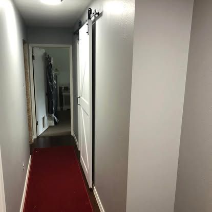 A hallway with light gray walls, a white barn door, and a red runner rug leading to another room.