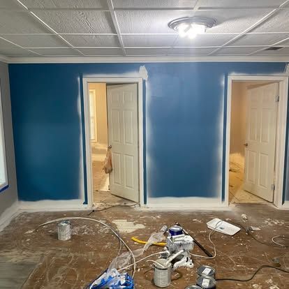 A room with freshly painted deep blue walls, two open white doors, and painting supplies scattered on the floor.