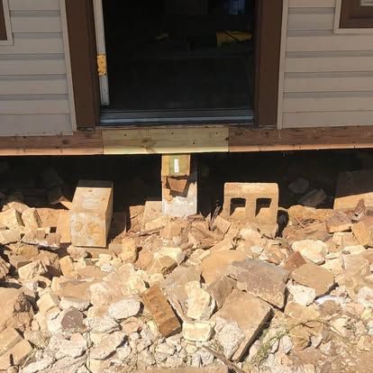 An elevated doorway of a house with a damaged foundation surrounded by a pile of loose concrete bricks and stone debris.