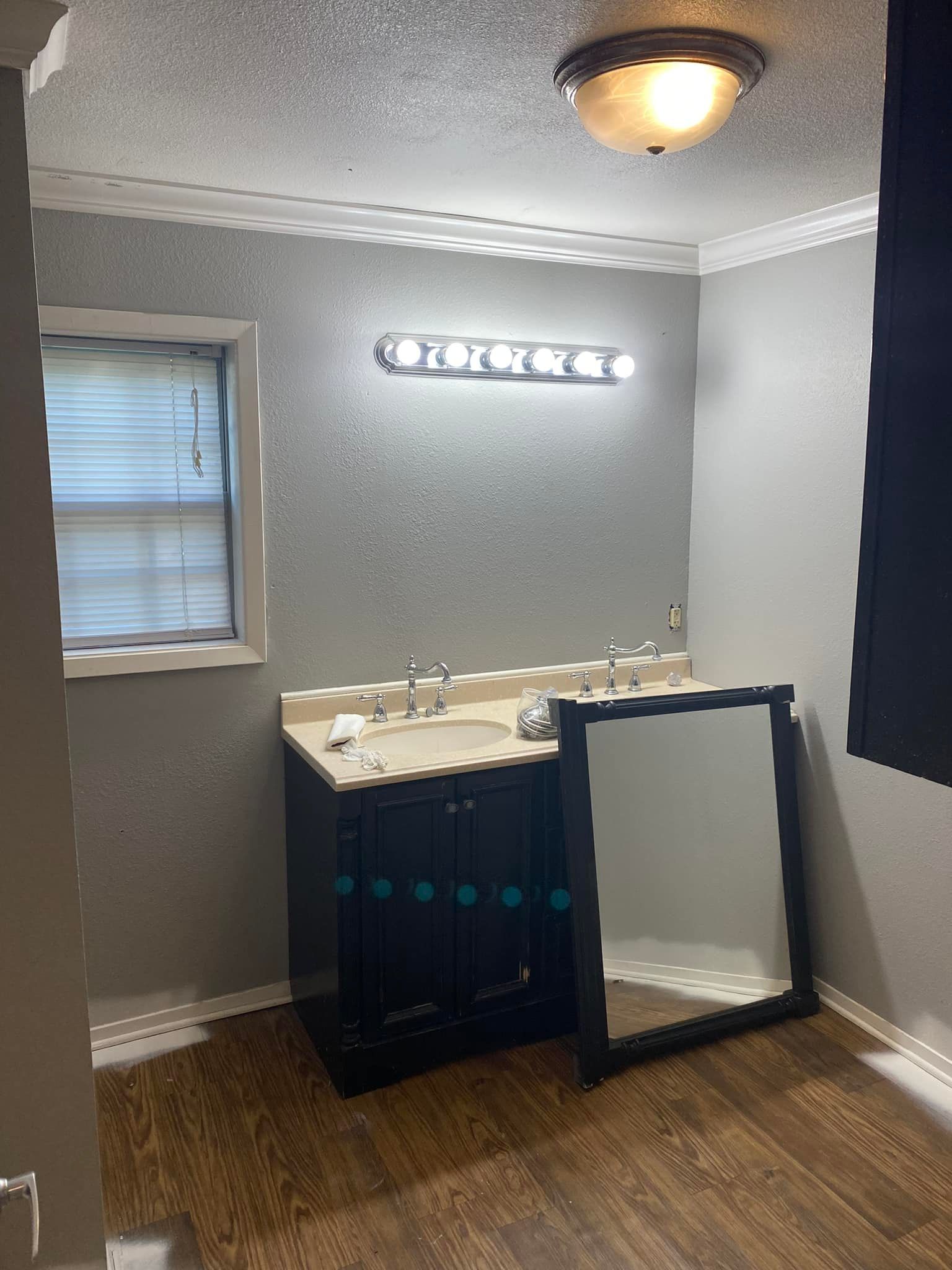 A bathroom vanity with a dark base and beige countertop stands against a gray wall, with a detached mirror on the floor.