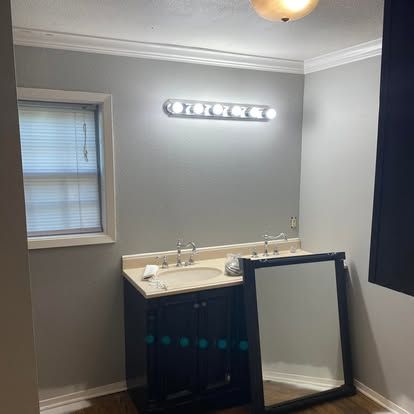 A bathroom vanity with a dark blue cabinet and sink, a vanity light, and a mirror leaning against the side.