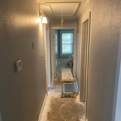 A hallway under renovation with light gray walls, an open door leading to a sunlit room, and a metal work platform.