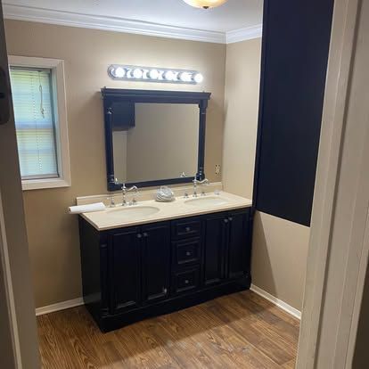 A bathroom vanity with a dark wood cabinet, a white double sink countertop, and a large mirror with a light fixture above.