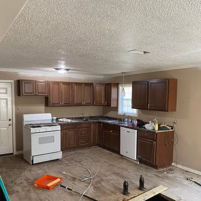 A kitchen under renovation with brown cabinets, a white stove, a white dishwasher, and wood-look flooring.