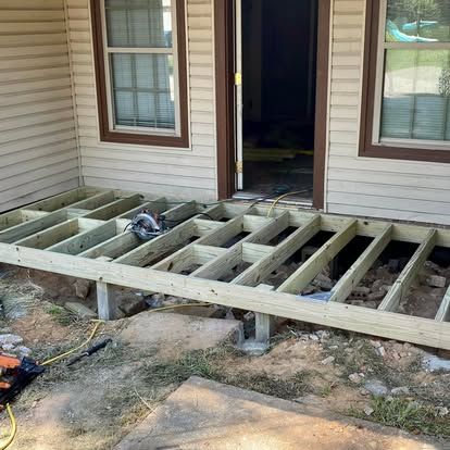 A partially built wooden deck frame attached to the front of a house, with a circular saw sitting on the joists.