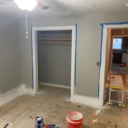 A room undergoing renovation with grey walls, taped door frames, and a portable workbench near an open doorway.