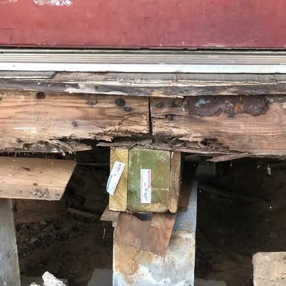 Decaying wooden deck framing supported by a new, mismatched green pressure-treated post on a concrete block foundation.