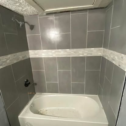 A shower and bathtub combination with gray rectangular wall tiles and a horizontal strip of white decorative accents.
