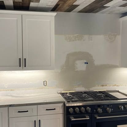 White kitchen cabinets and drawers with a gas stove and an unfinished tiled backsplash area in a residential kitchen.