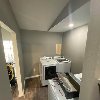 A laundry room with a grey wall, white washer and dryer, wood flooring, and a painting tray in the foreground.